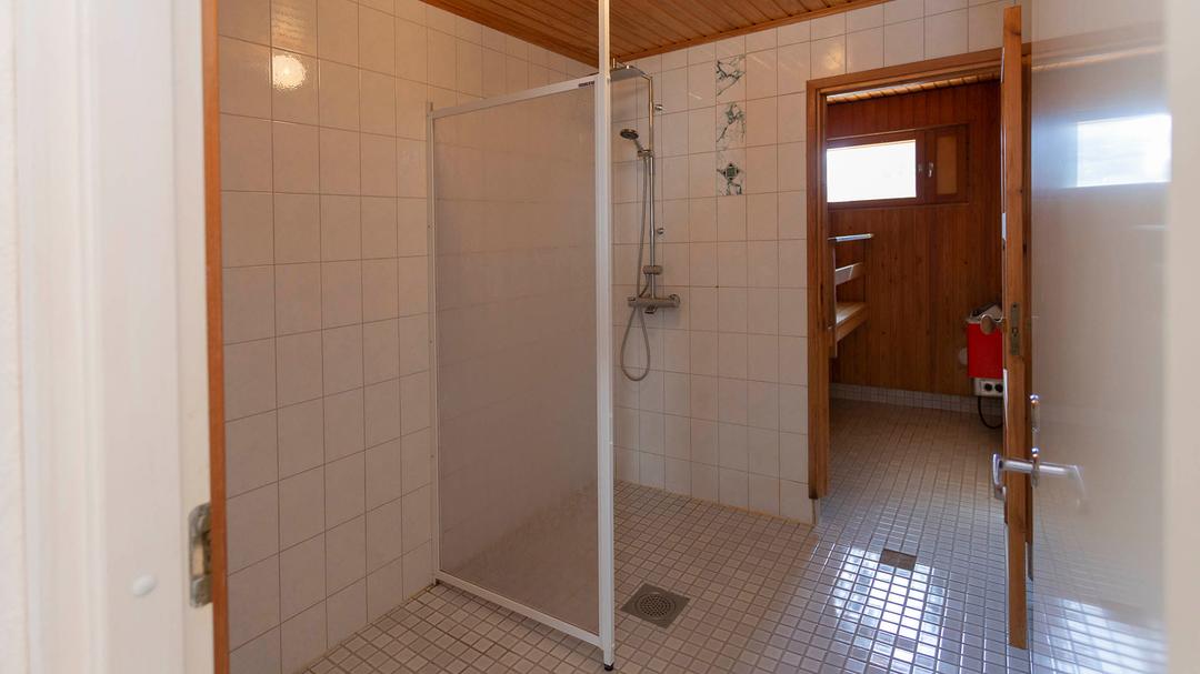 pesuhuone jossa suihkun edessä suihkuseinä ja taustalla saunan ovi on auki