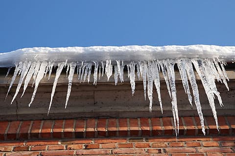 Jääpuikkoja tiilisen rakennuksen räystäällä taustalla sininen taivas
