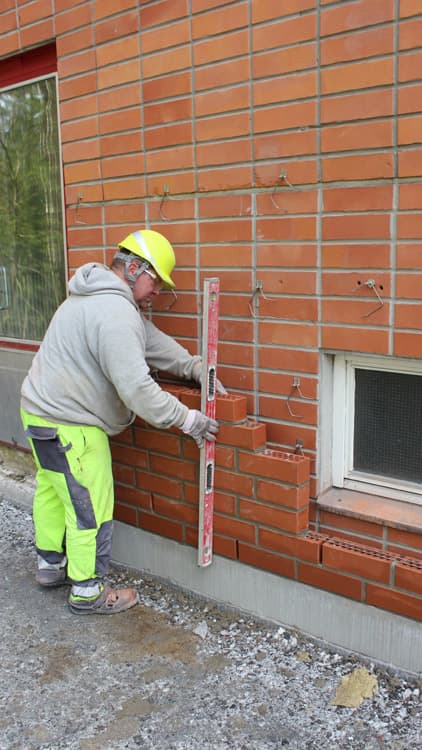 Uuden julkisivun muuraustyöt olivat ennen kesää jo hyvässä vauhdissa. Vanhan betonielementtikuoren sidontaa vahvistettiin pulttaamalla kuoret taustarakenteeseen ja julkisivumuurausta varten asennettiin vanhaan ulkokuoreen ns. liikkeen sallivat tiilisiteet, esittelee vastaava mestari Seppo Pahkala.