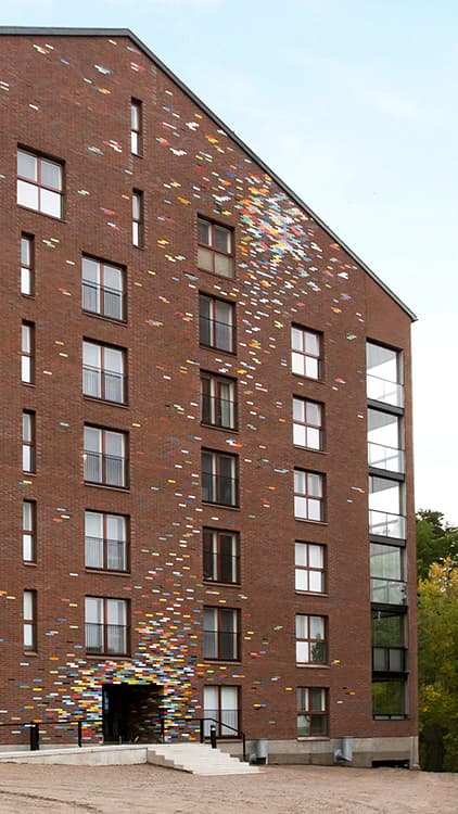 <p data-block-key="qode9">Lasitettujen tiilien väriskaala antaa runsaasti mahdollisuuksia talon julkisivujen kirjailuun. Kuvan talo on Jyväskylän Kankaan alueella sijaitsevasta As.Oy Albertinpihasta, johon kuvataiteilija Mika Natri on suunnitellut lasitiilistä tehdyn värikkään installaation</p>