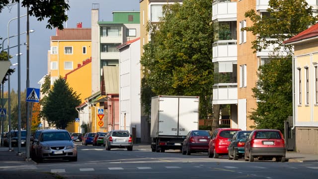 autoja parkkeerattu kadunvarteen kerrostalojen edessä