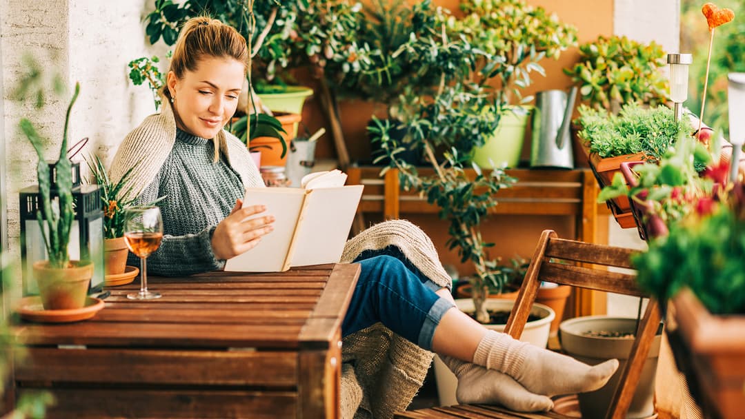 nainen istuu parvekkeella ja lukee kirjaa. Parveke on sisustettu runsailla kasveilla