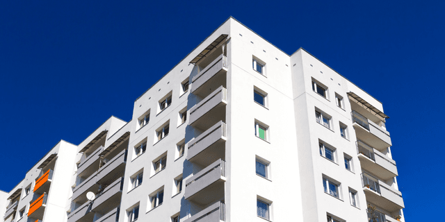 Kuva valkoisesta kerrostalosta, jossa on parvekkeita ja taustalla on sininen taivas
