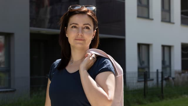 Nainen tummassa paidassaan seisoo kerrostalojen edessä