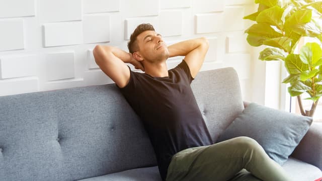 Mies istuu harmaalla sohvalla taustalla valkoinen seinä nauttien raikkaasta sisäilmasta swegon