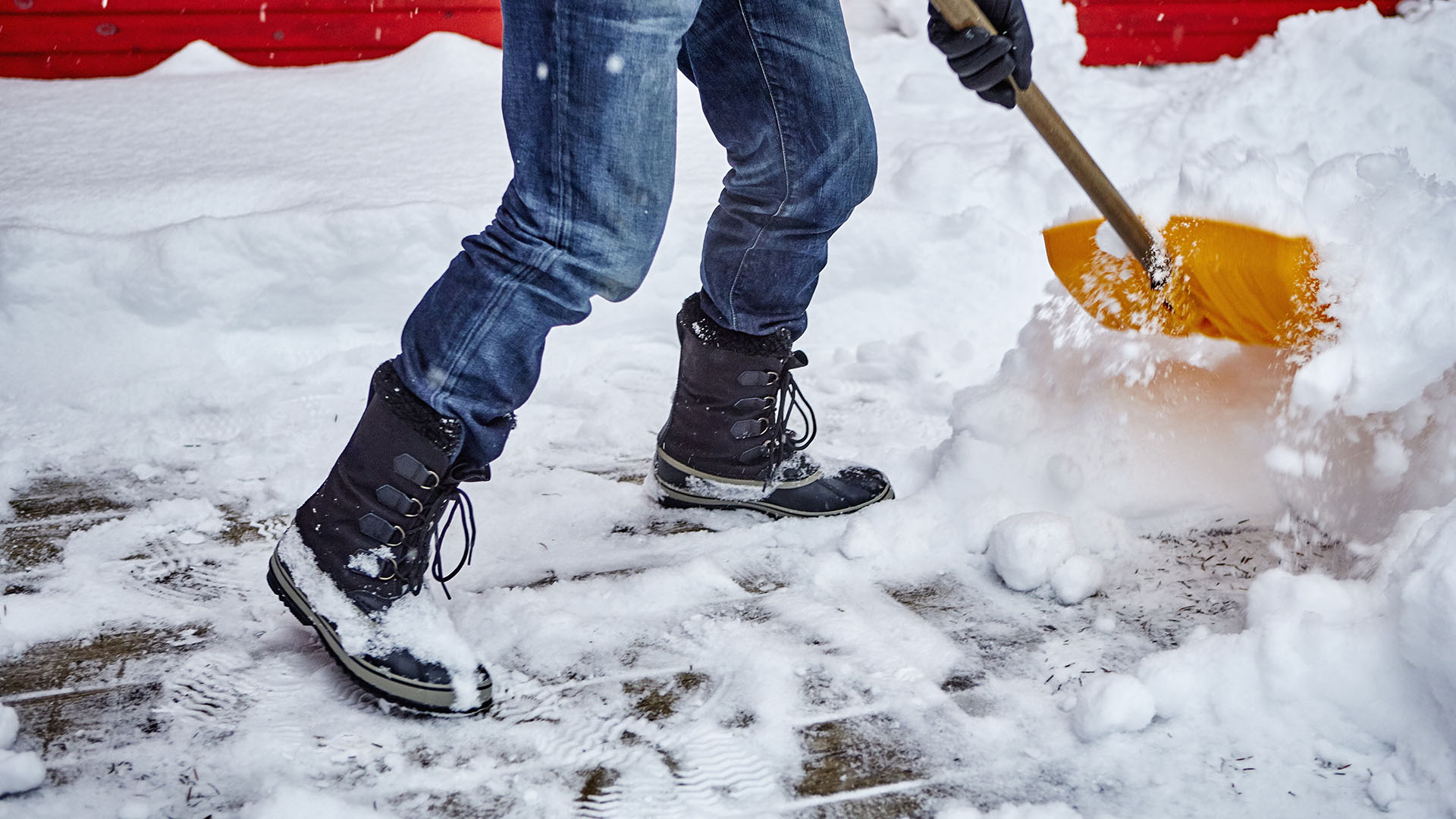 Mies lapioi lunta lumilapion avulla pihakiveyksen päältä
