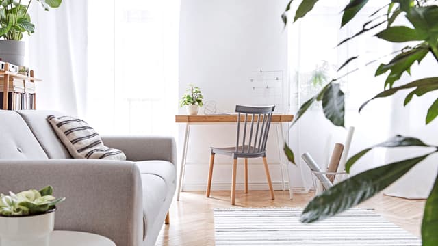 tyylikäs skandinaavinen olohuone, jossa vaalean harmaa sohva ja taustalla kirjoituspöytä puisine tuoleineen