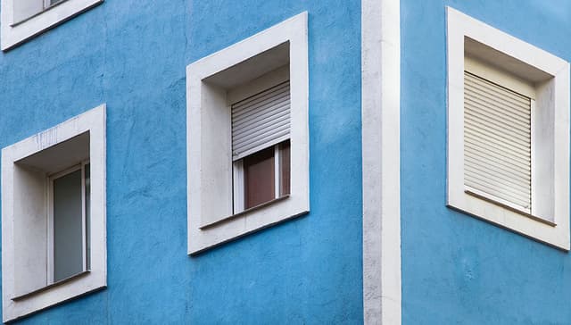 vaaleansinisellä värillä maalattu rapatun kerrostalon kulmaa, jossa valkoisella maalilla maalatut ikkunanpielet Smartvatten