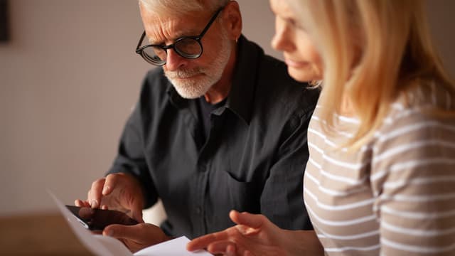 vanhempi mies ja nainen tutkivat kännykkää sekä papereita Geonovan maalämpöopas auttaa