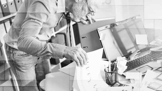 mies etsii sotkuiselta pöydältä asiakirjoja