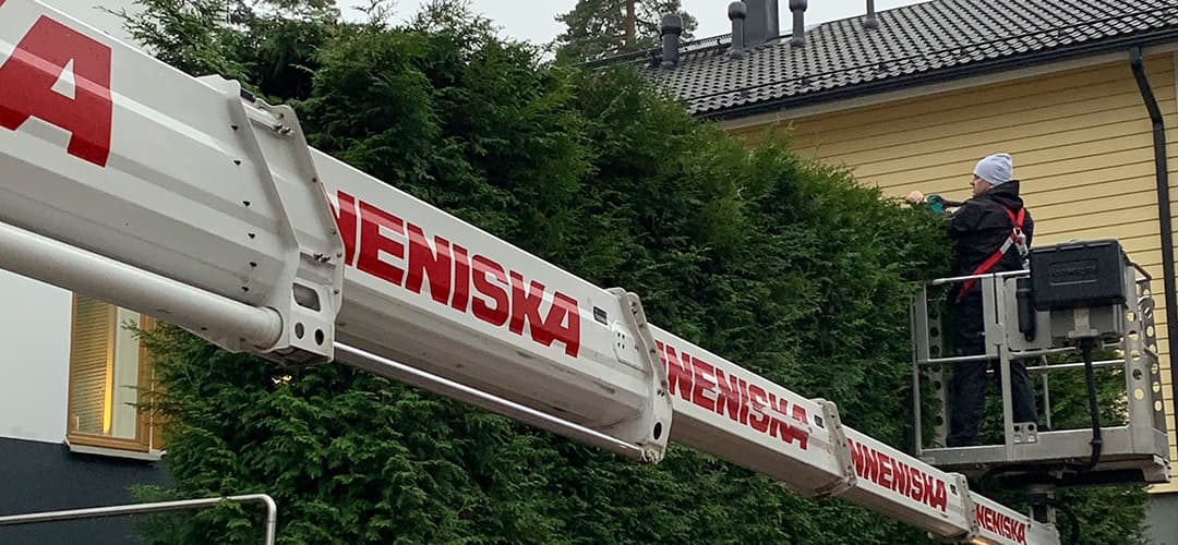 henkikö leikkaa korkeaa tuija-aitaa henkilönostimen korista turvallisesti