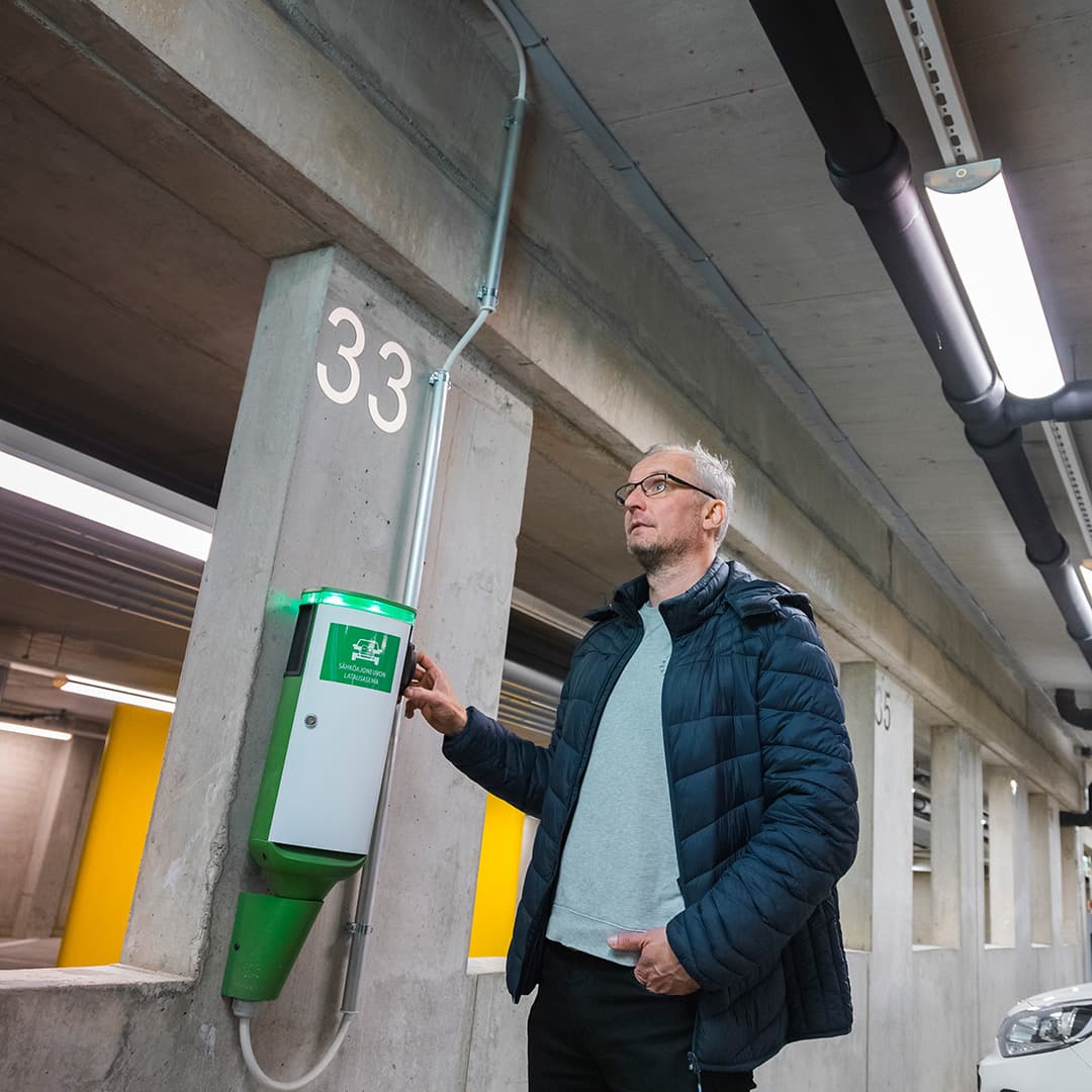 Taloyhtiön isännöitsijä taloyhtiön parkkihallissa näyttämässä miten sähköauton latauspaikka on asennettu