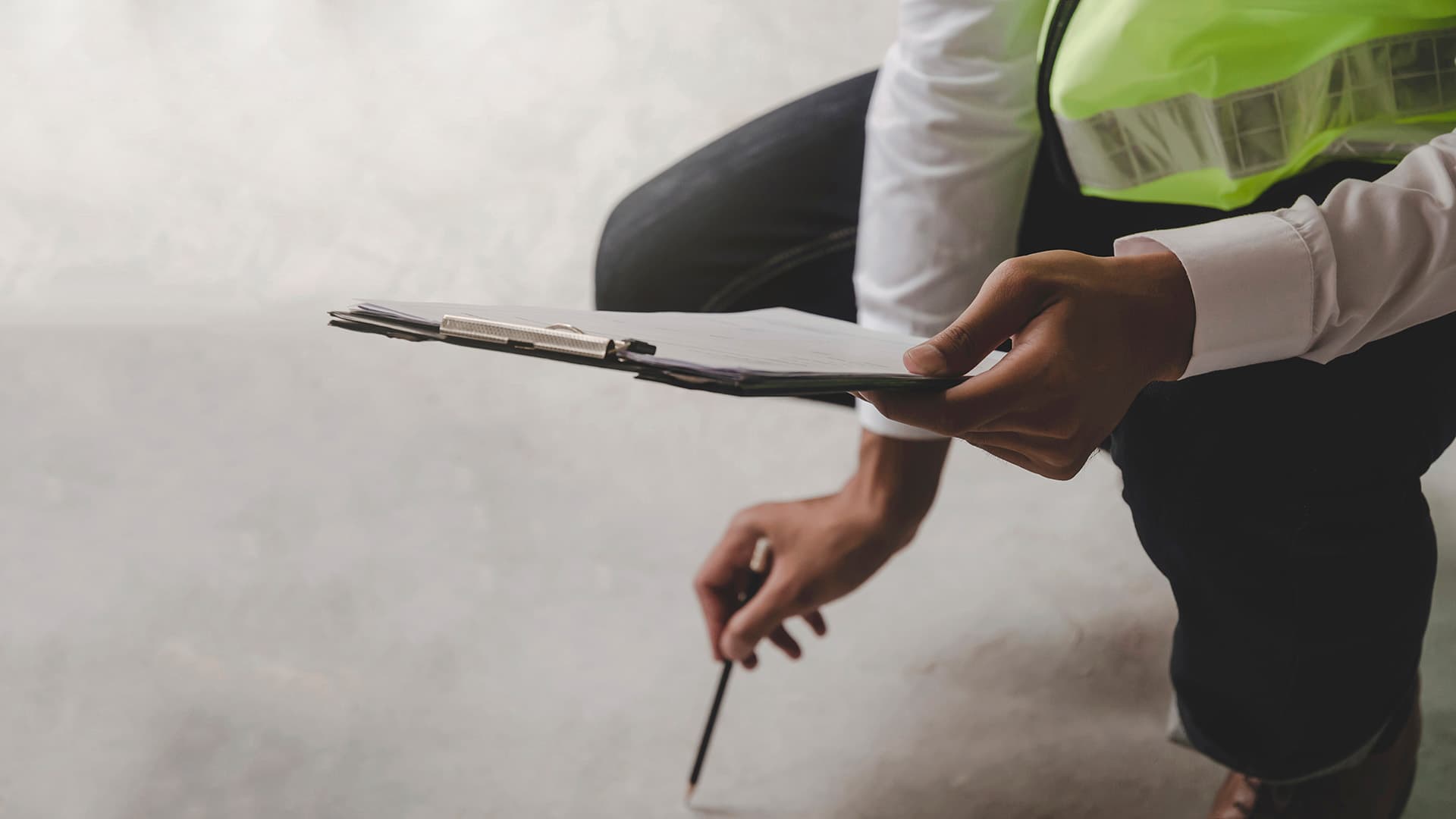 mies osoittaa kynällä betonilattiaa ja kädessä hänellä on tarkastusraportti